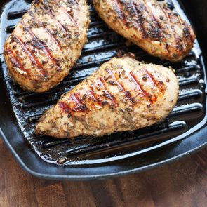 Chicken breasts grilling in a black cast-iron skillet on a wooden surface, showing grill lines and herb seasoning.