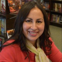 A person smiles while sitting in a bookstore, surrounded by shelves filled with books.