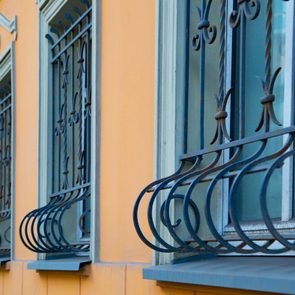 Ornate wrought iron bars frame blue windows on an orange building facade, creating a rhythmic pattern along the wall.