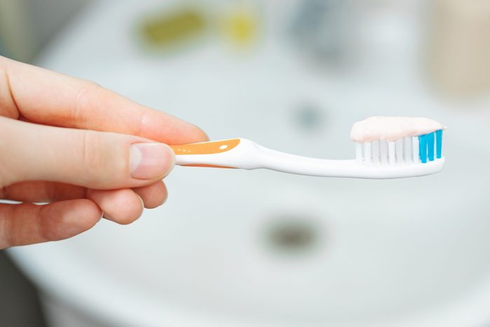 Hand holds a toothbrush with toothpaste on bathroom background, close up view.