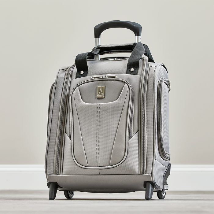 A grey wheeled suitcase stands upright with an extended handle in a neutral-toned room.