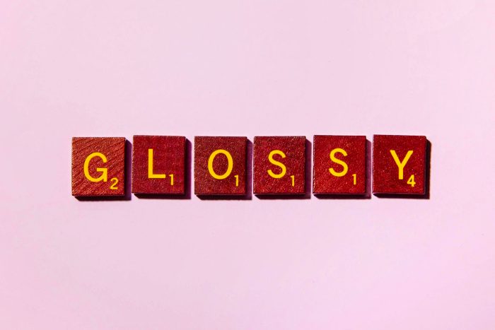 word GLOSSY in scrabble tiles on pink background