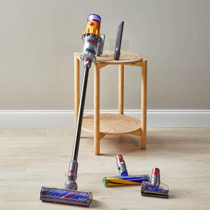 Vacuum cleaner stands near a wooden side table with attachments on a light-colored floor, in a minimalist room.