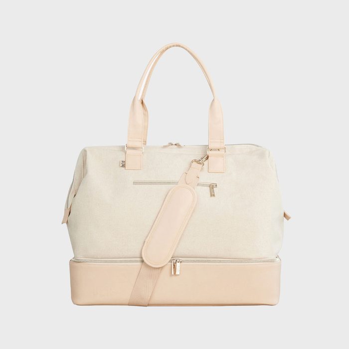 A beige travel bag with tan handles and shoulder strap; features a front pocket and bottom compartment, set against a plain background.