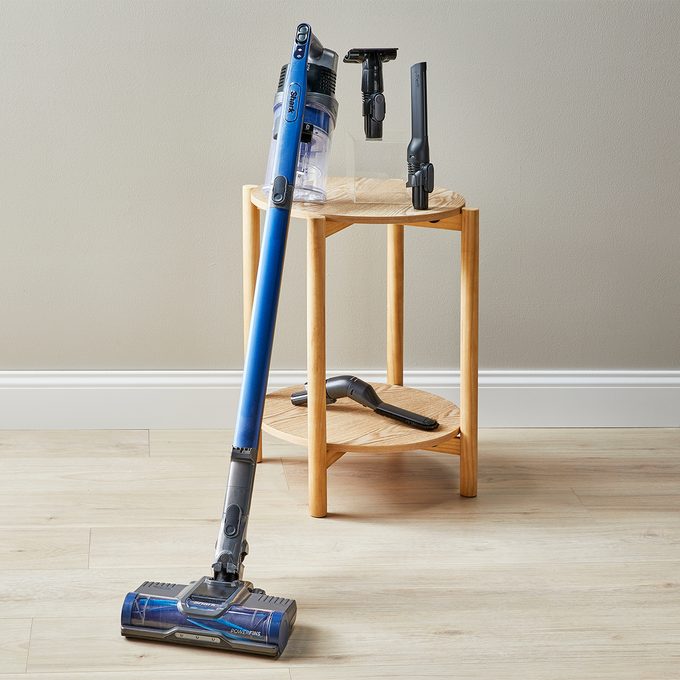Vacuum cleaner stands on a wooden floor, leaning against a small wooden table with attachments placed on top.