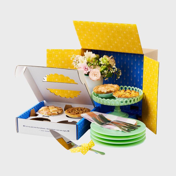 Pies rest in an open decorative box and on a green plate stand; nearby are stacked green plates, cutlery, and a floral arrangement.