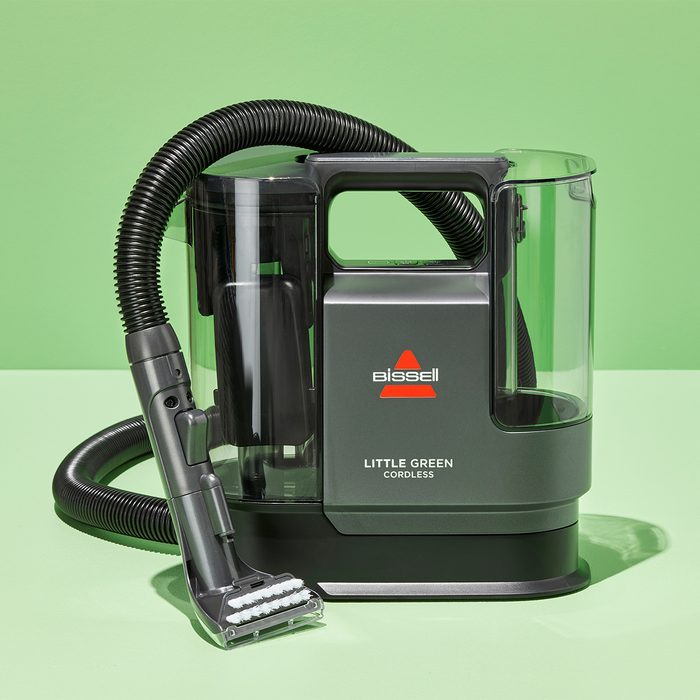 Vacuum cleaner sits upright on a green surface, featuring a hose and transparent tank. Bold text reads: 