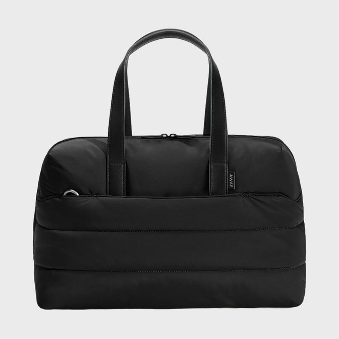 A black duffel bag with handles rests against a plain, light background, showcasing a side pocket and subtle branding tag.