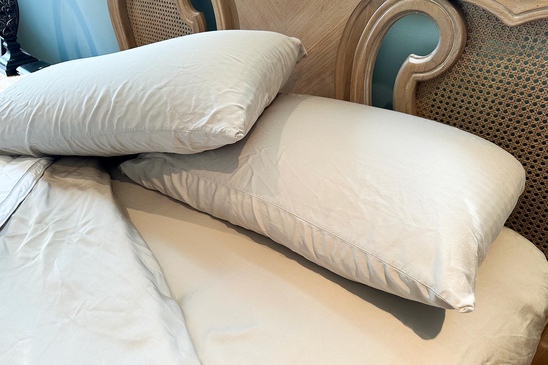 Two cream pillows rest on a bed with a wooden headboard featuring intricate cane detailing in a softly lit room.