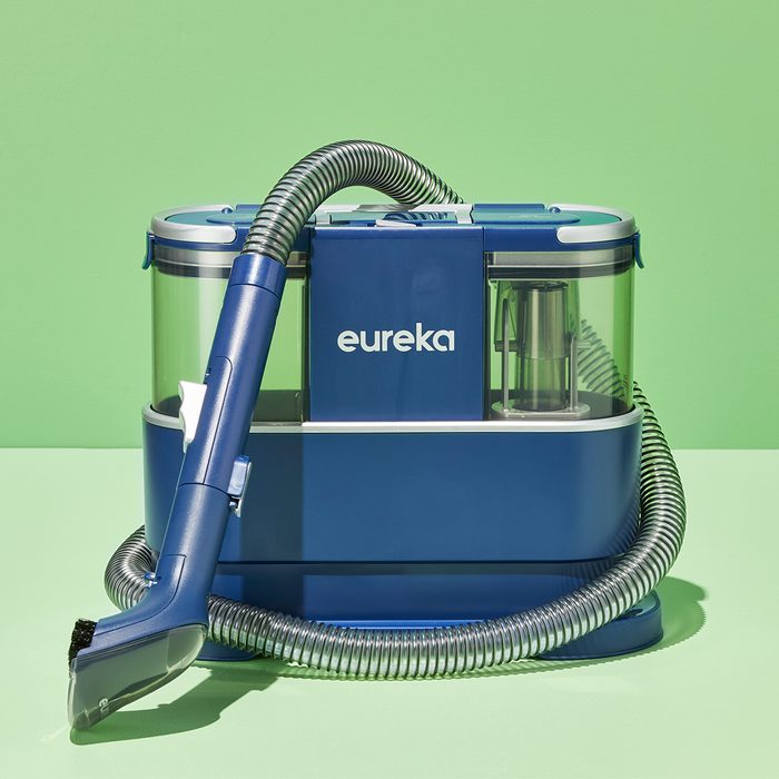 Blue vacuum cleaner sits with hose attached, displayed against a vibrant green background. The word 