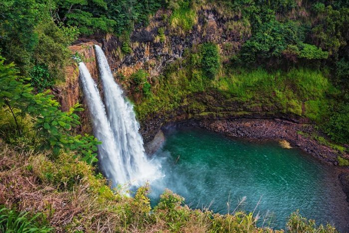 Waterfall cascades into a turquoise pool, surrounded by lush greenery and rocky cliffs.