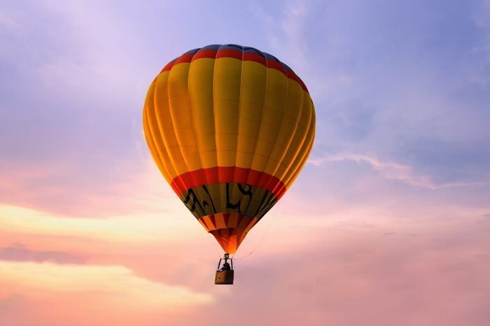A hot air balloon ascends in the sky, surrounded by a colorful sunset backdrop with hues of orange and purple.