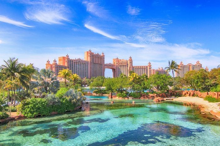 Resort towers overlook a tropical landscape with clear blue water, lush greenery, and palm trees under a bright, clear sky.