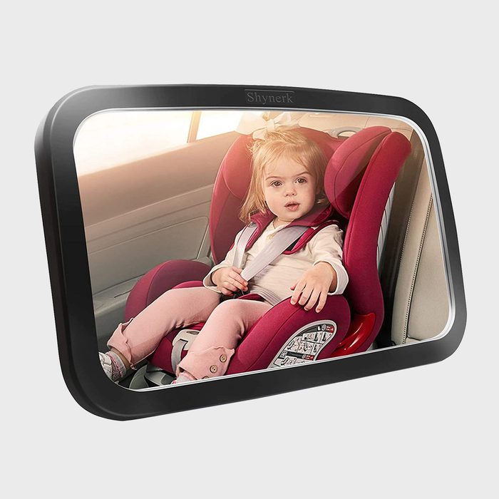 Mirror reflects child seated in red car seat, wearing a seatbelt, inside a vehicle; the brand name 