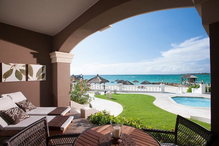 Lounge chairs sit under an archway, overlooking a pool and vibrant ocean view, with thatched umbrellas and lush greenery enhancing the tropical setting.