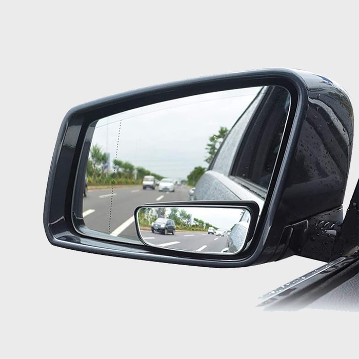 Car side mirror reflects road with moving vehicles, trees along the edge, and overcast sky.