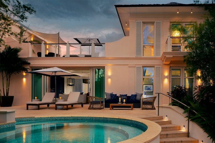 House overlooks a pool, with lounge chairs and an umbrella on the patio; evening lights create a cozy, tropical atmosphere.