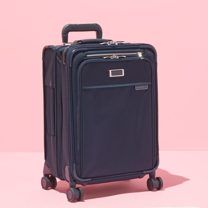 Suitcase standing against a pink background, featuring four wheels, a telescopic handle, and outer zippered compartments.