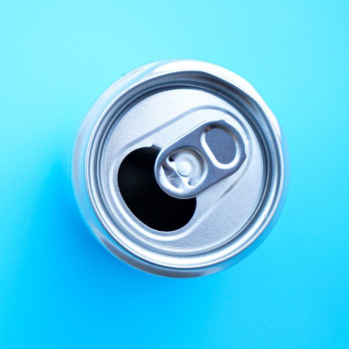 Soda can sits with open tab on a bright blue background.