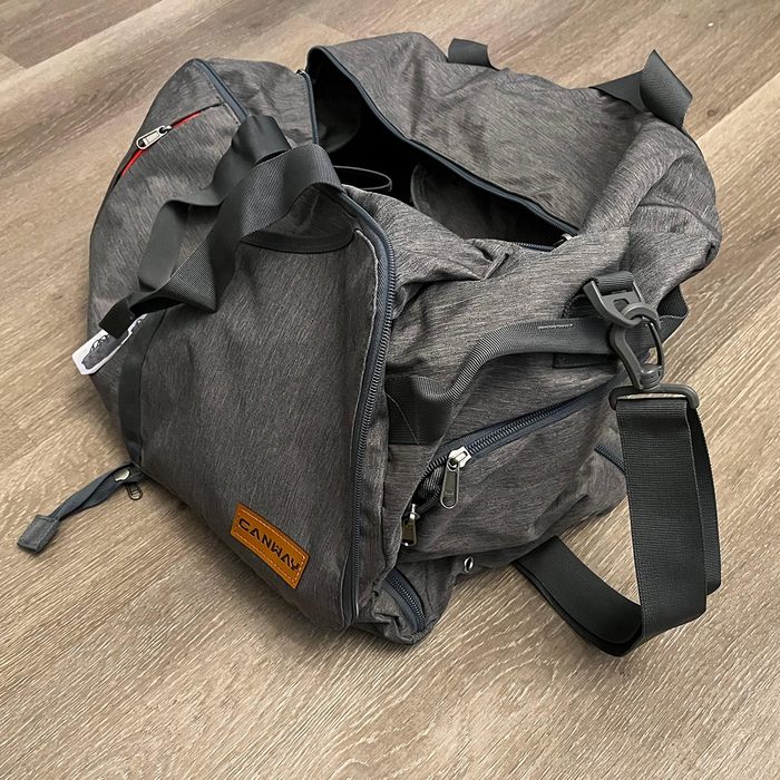 Bag sits open on wooden floor, displaying multiple compartments. A visible label reads 