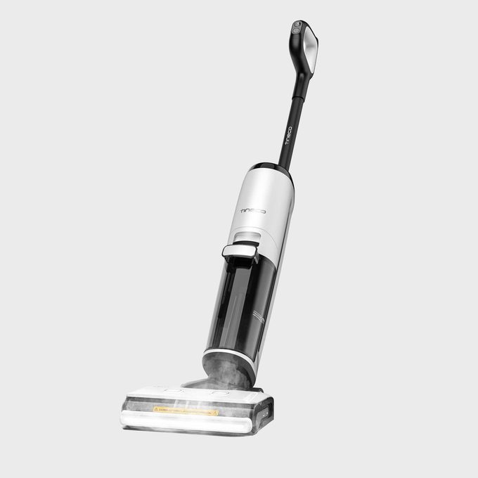 Vacuum cleaner stands upright on a white background, displaying sleek design with visible transparent dustbin and controls on the handle.