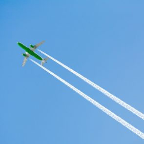 Green airplane soaring, leaving white contrails against a clear blue sky.