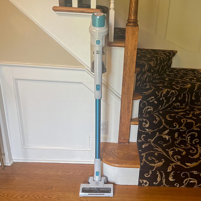 Vacuum cleaner leaning against carpeted stairs; nearby walls and hardwood floor provide a domestic setting.
