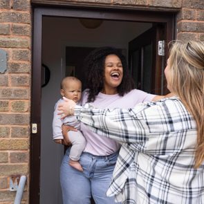 Woman holding a baby greets another woman at a doorway. Plaque with 