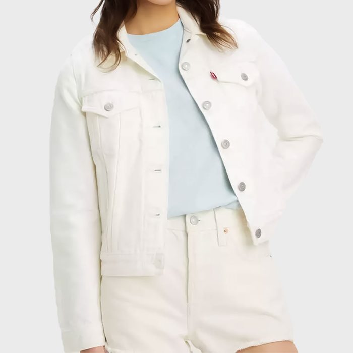 A person wears a white denim jacket and shorts with a light blue shirt against a plain background.