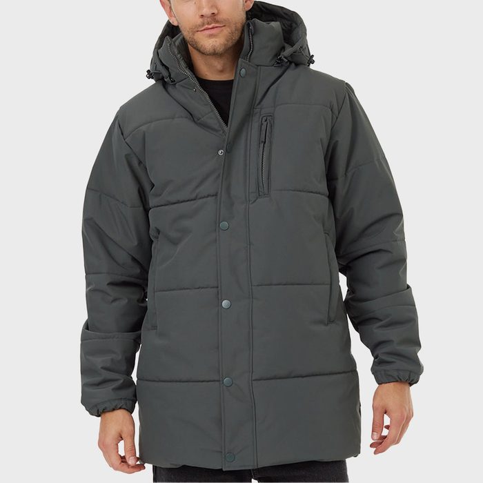 A man wears a dark gray hooded winter coat, standing calmly against a plain white background.