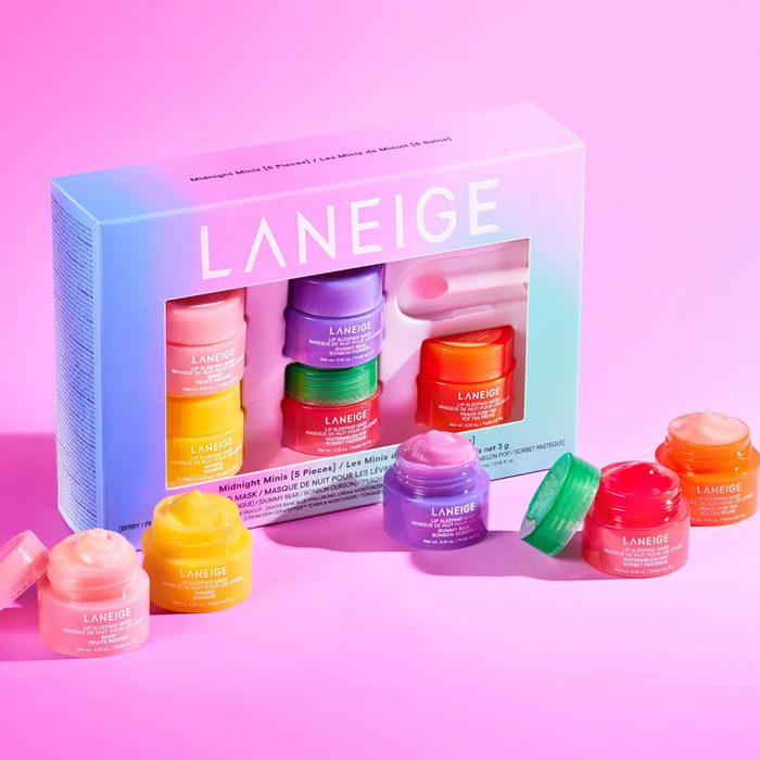 Colorful cosmetic jars displayed beside their box on a pink surface. Box reads 