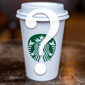 A white coffee cup with a green logo and large question mark sits on a wooden surface, blurry background.