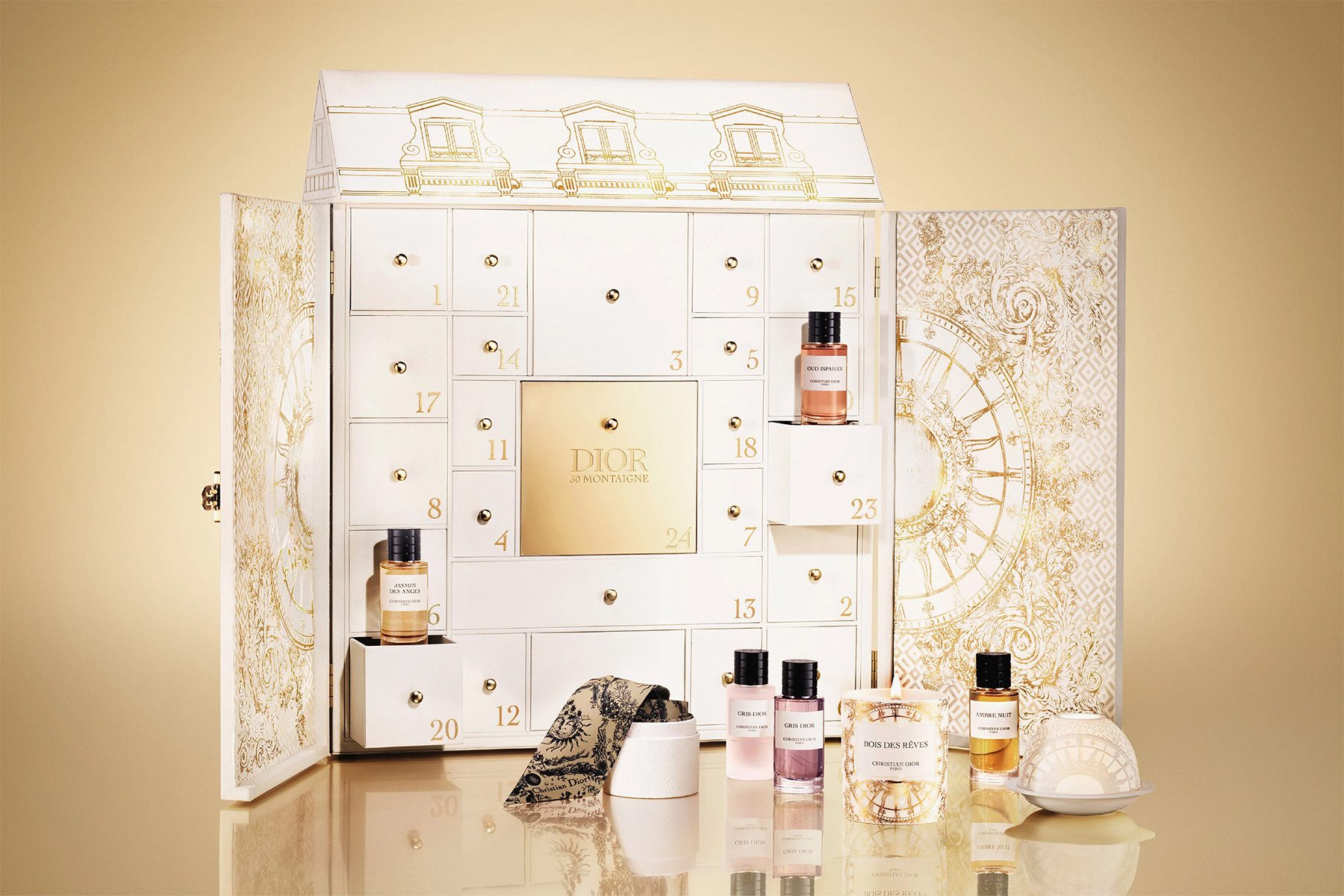 A white advent calendar holds small bottles, displayed on a reflective surface, with ornate gold patterns and "DIOR 30 MONTAIGNE" text.