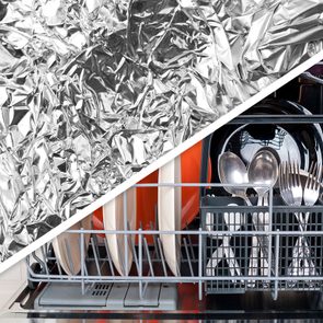 Crinkled aluminum foil overlaps a dishwasher loaded with plates, spoons, and forks, creating a juxtaposition of textures and kitchen objects.