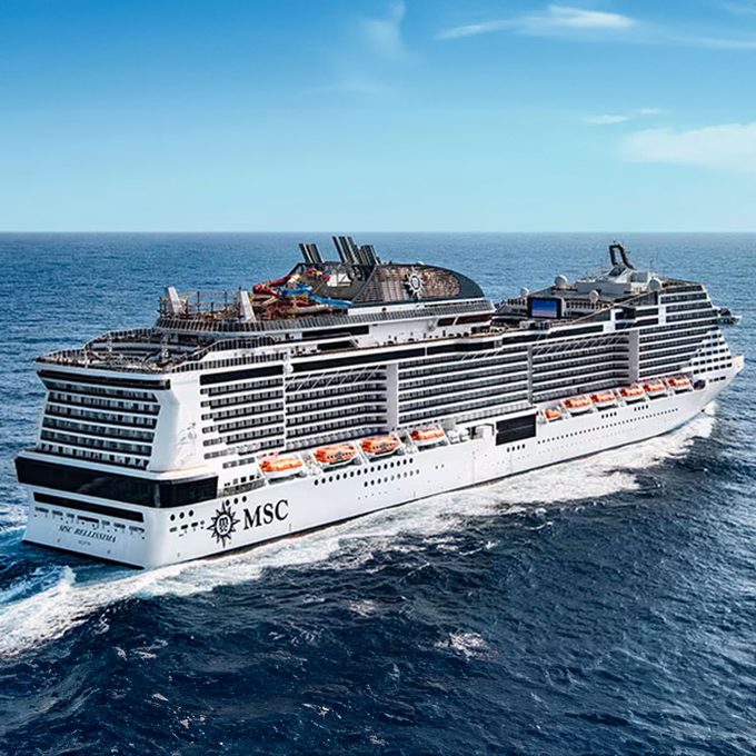 A large cruise ship sails across the open ocean under a clear blue sky, displaying 