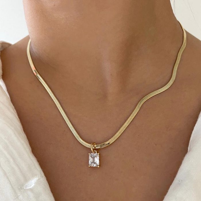 Necklace displays a rectangular pendant, worn around a person's neck, against a light fabric background.