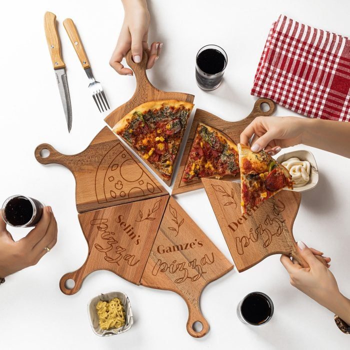 Pizza slices being served on engraved wooden boards; people dining with drinks, utensils, and red checkered napkin nearby.