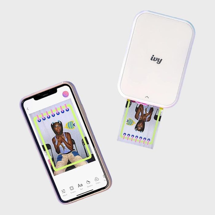 Printer ejects photo from smartphone app, displaying colorful picture of person in decorative frame; both devices on light gray background.
