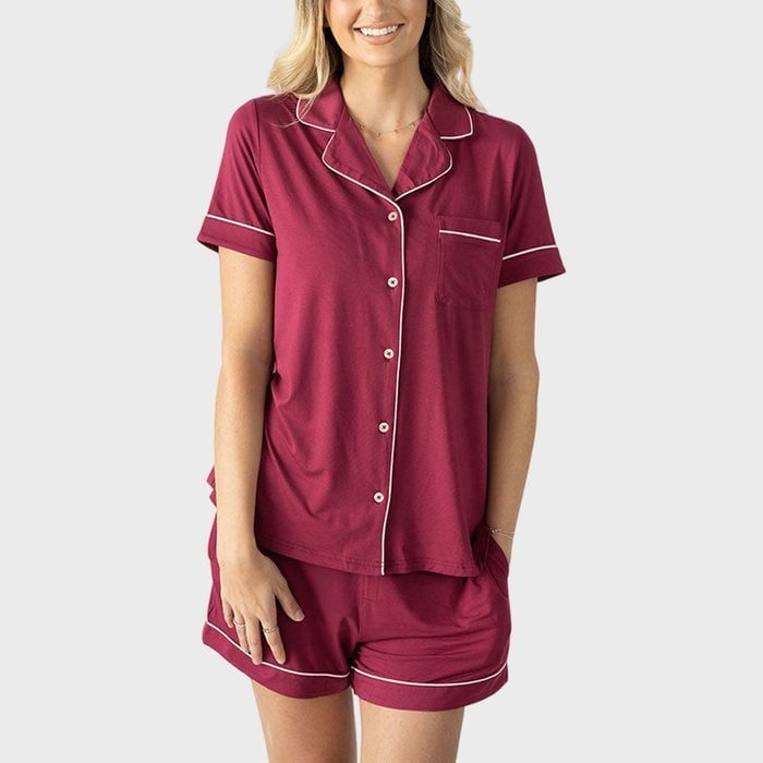 A person wearing a burgundy pajama set with white piping, standing against a plain grey background.