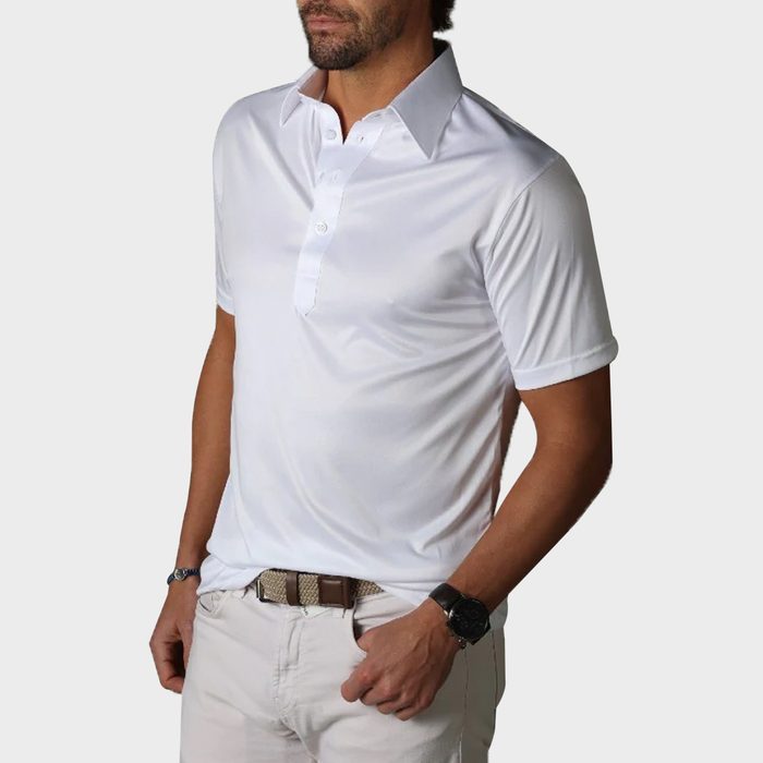 A man wears a white collared shirt, standing with hands relaxed, set against a plain light background.