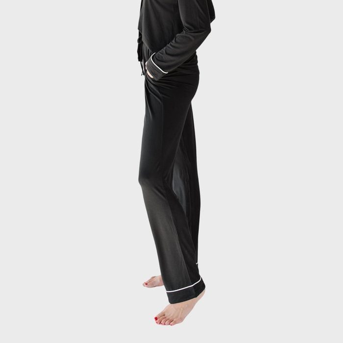 Person stands in black pajamas with white cuffs, hands in pockets, isolated on a plain gray background.