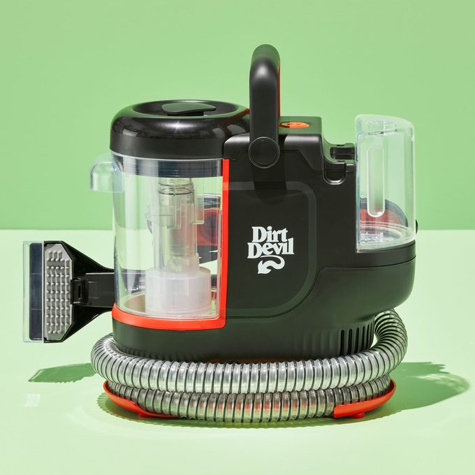 Vacuum cleaner on a green background, displaying transparent compartments and coiled hose, labeled 