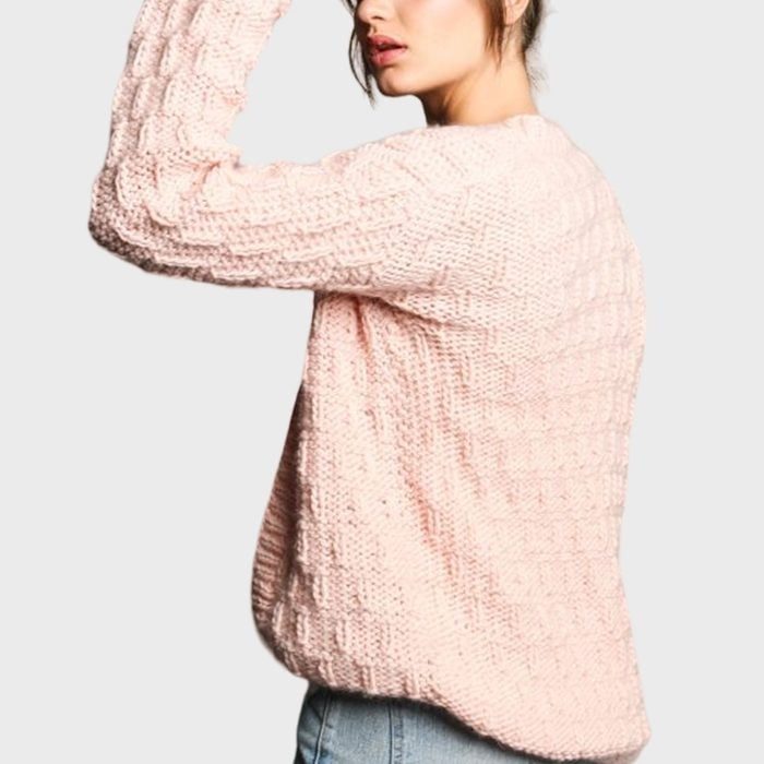Pink sweater draped on a person, shown from the side, against a plain light background. The person wears light blue jeans.