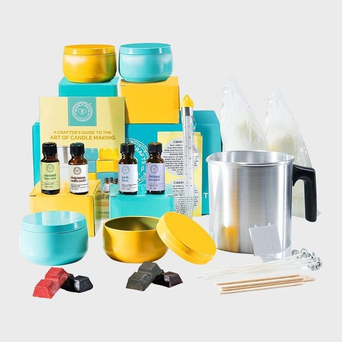 Candle-making kit displayed with colorful containers, essential oils, wax blocks, and tools; surrounded by packaging and instructional materials.