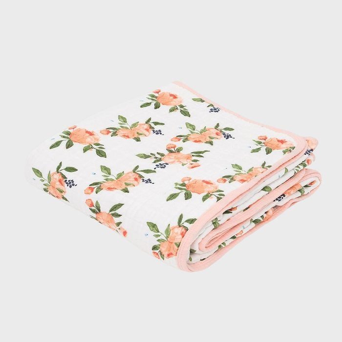 A folded quilt displays a floral pattern on a white background, featuring pink flowers and green leaves.