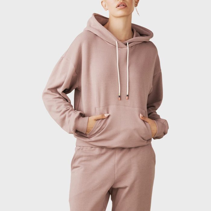 A person wears a light brown hoodie and matching joggers, standing against a plain, light gray background.