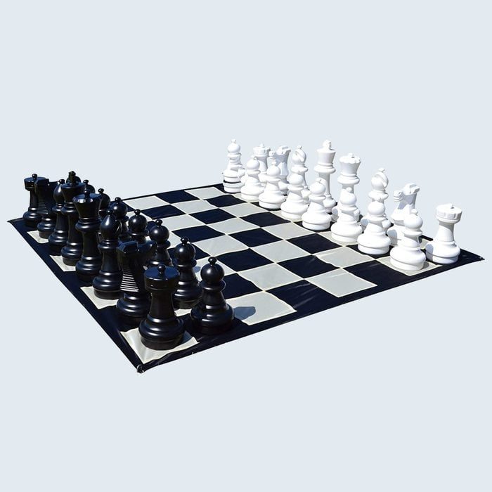 Giant chess pieces are set up on a large checkered mat, positioned for starting a game in an open space.