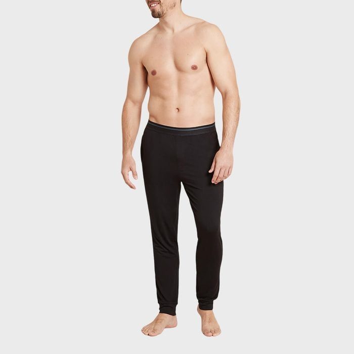 Shirtless man wearing black pants stands smiling against a plain gray background.