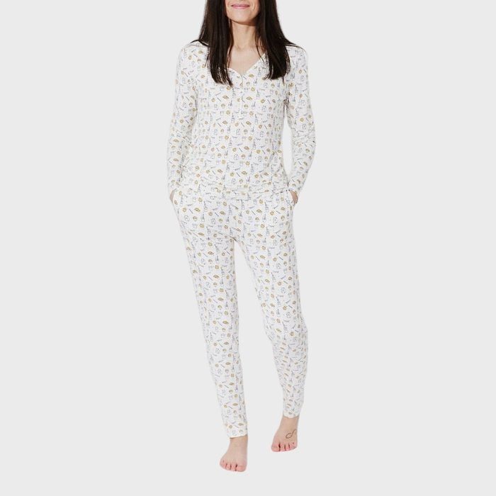 Person wearing patterned pajamas stands barefoot on a plain, light-colored background, hands in pockets, relaxed posture.