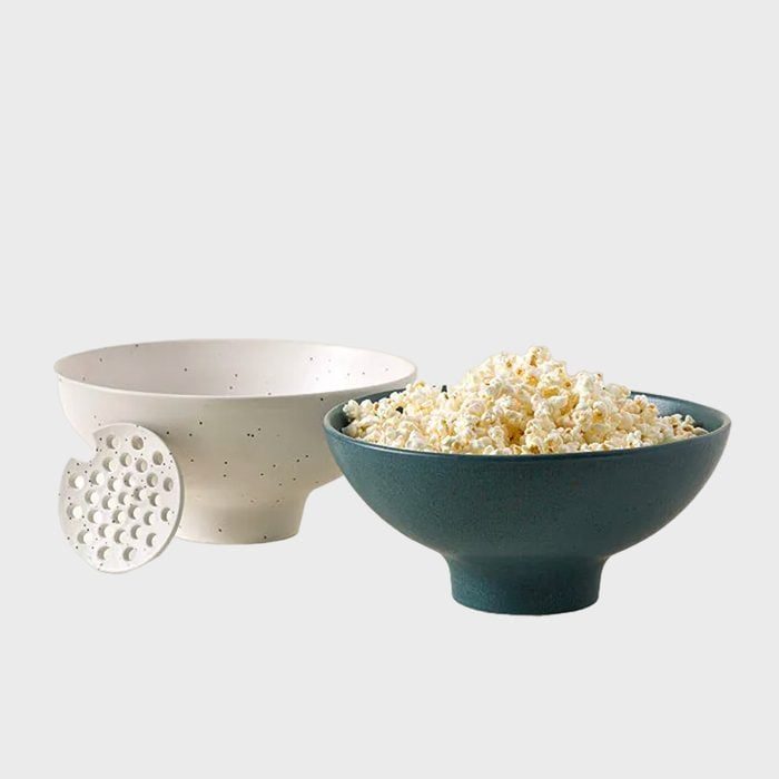 Blue bowl holds popcorn, surrounded by a white bowl and a perforated disc, on a plain background.